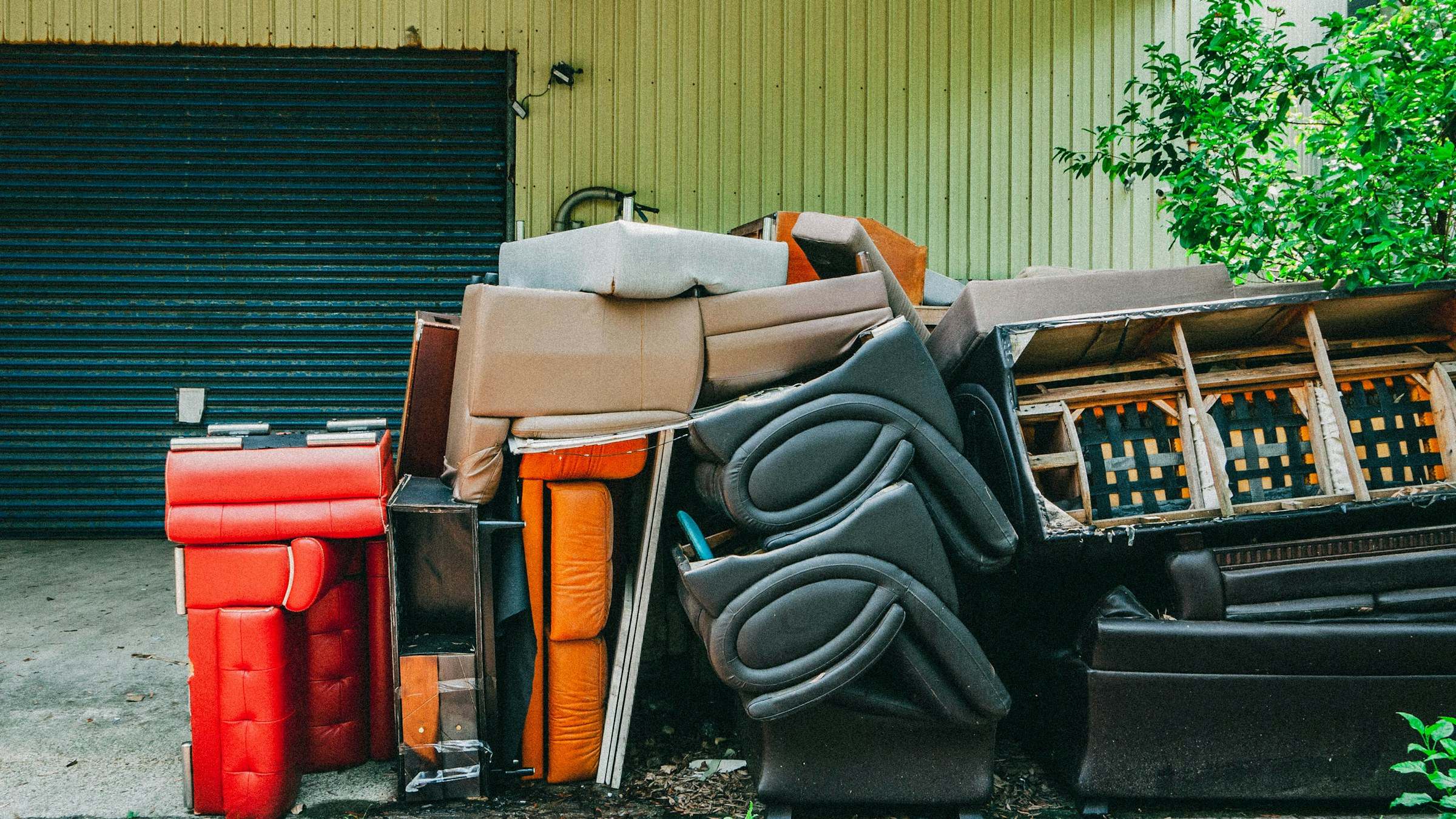 Old couches, chairs and cabinets piled in front of a garage door