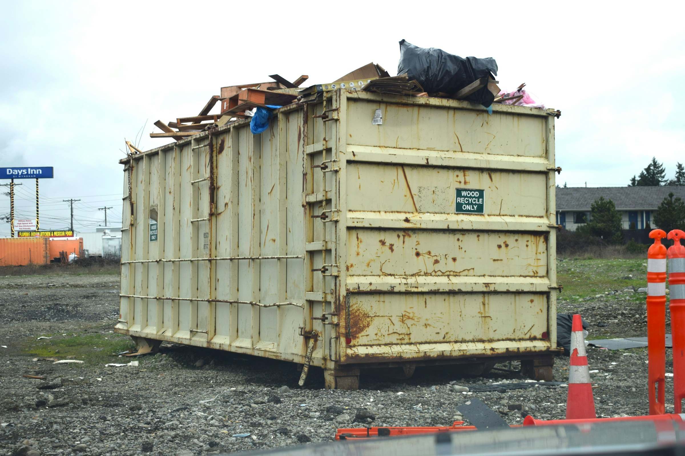 A loaded roll-off dumpster on a gravel lot, traffic cones beside it